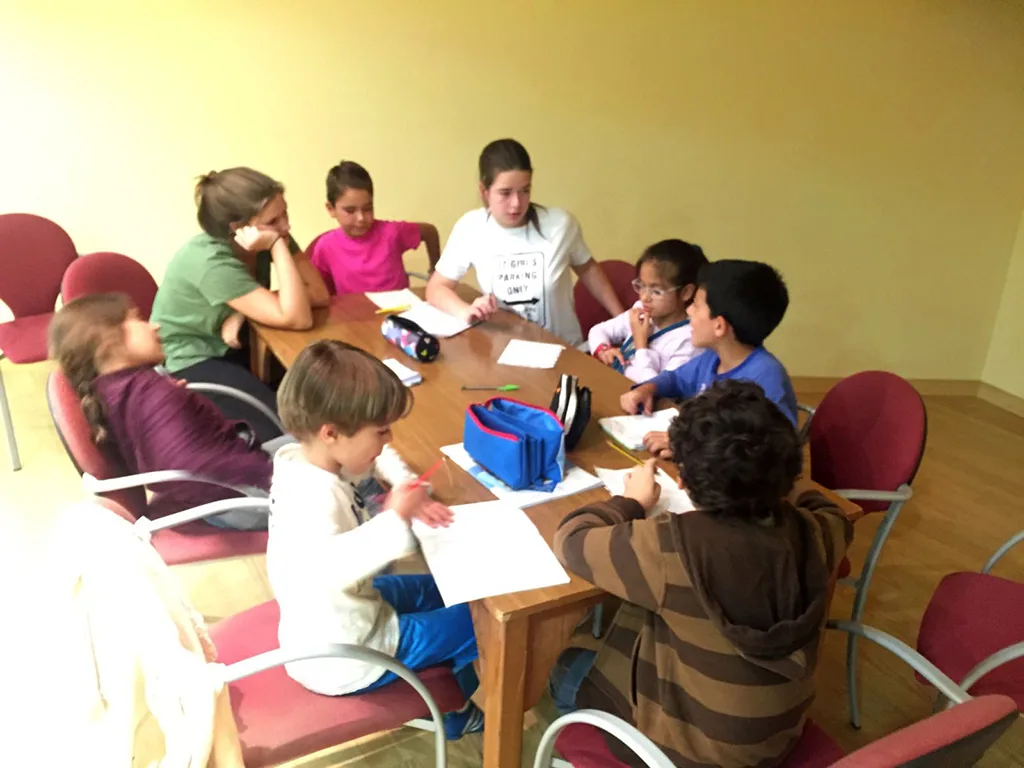 Jugendliche betreuen Kinder an Gruppentischen im Klassenraum.